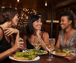 three-female-friends-eating-dinner-together-at-a-r-PTRGD3R-scaled.jpg